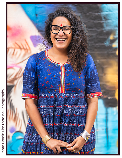Rakhee wearing a blue patterned dress with a colorful background