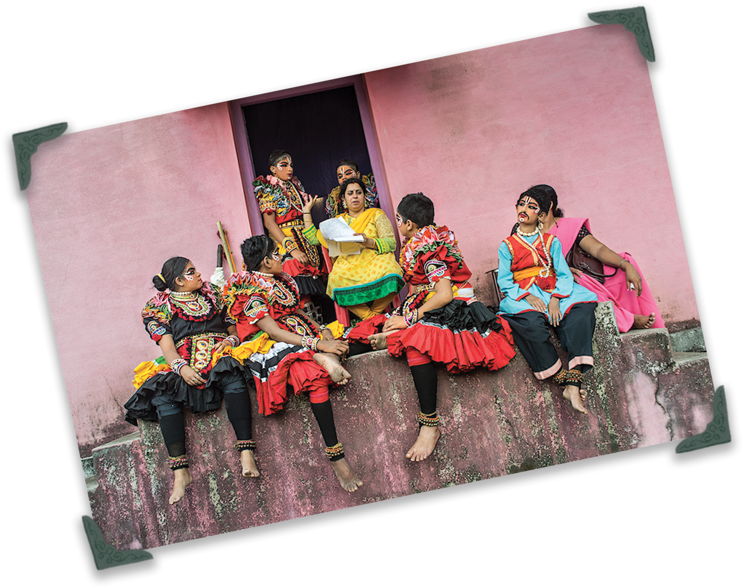 Group of students in colorful traditional attire sitting on a ledge against a pink wall. Credit: Richa C Bhavanam